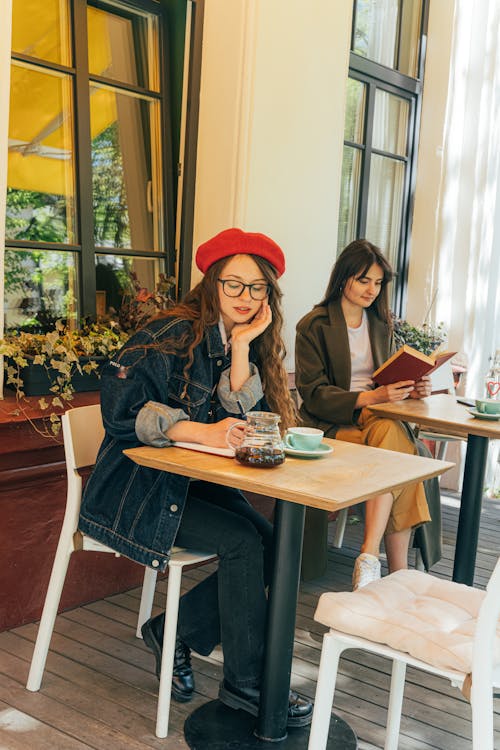 A Woman Writing on a Notebook and a Woman Reading a Book