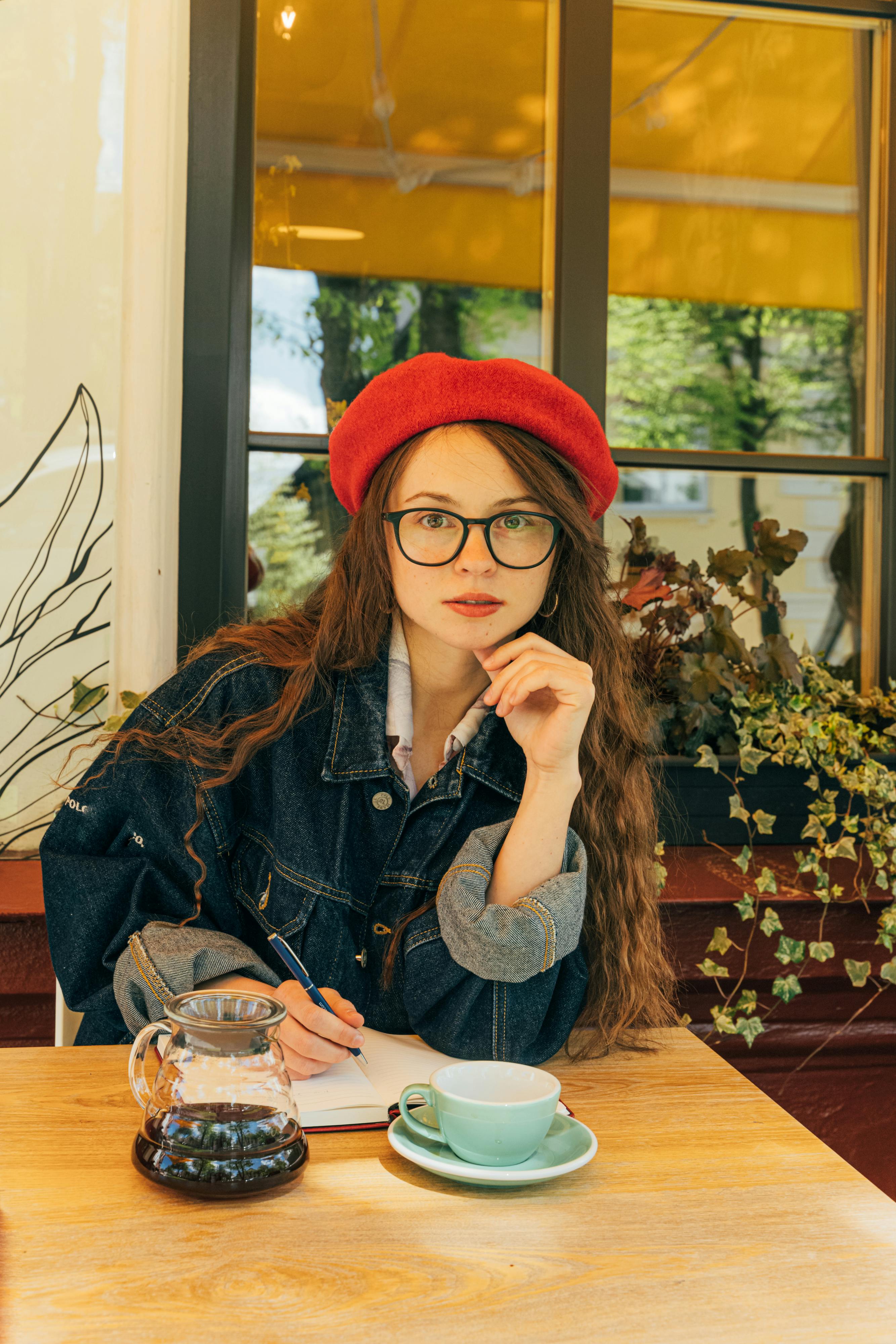 一位戴着红色贝雷帽和眼镜的时尚女性，正坐在咖啡桌旁，手里拿着咖啡和笔记本