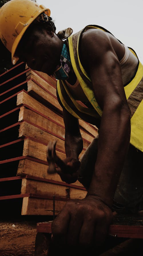 From below of African American man in helmet with hammer building house at work