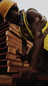 From below of African American man in helmet with hammer building house at work