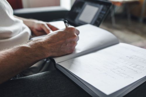 Free Focused individual writing notes in a notebook with a laptop nearby. Stock Photo