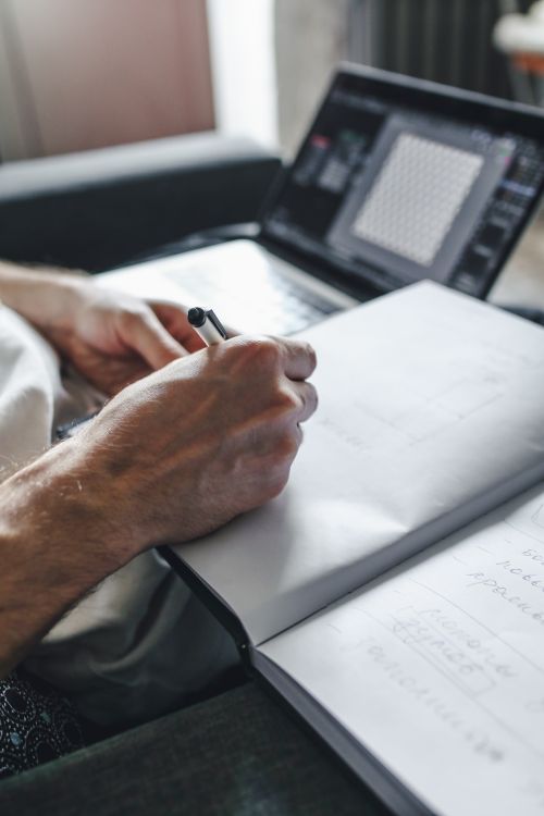 Free A close-up image of hands writing in a notebook, with a laptop in the background. Stock Photo