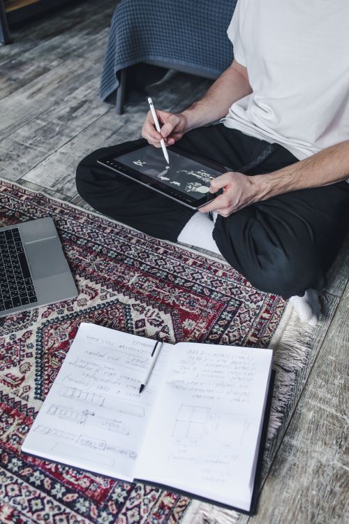 Free Person sketching on a digital tablet while sitting on a patterned rug indoors. Stock Photo