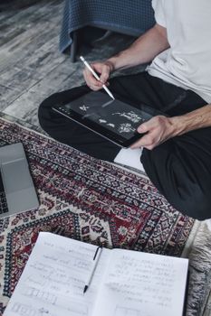 A person using a digital tablet and stylus for drawing while sitting on a patterned rug indoors.