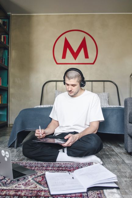 Young man sitting on floor with tablet and headphones in cozy urban bedroom.
