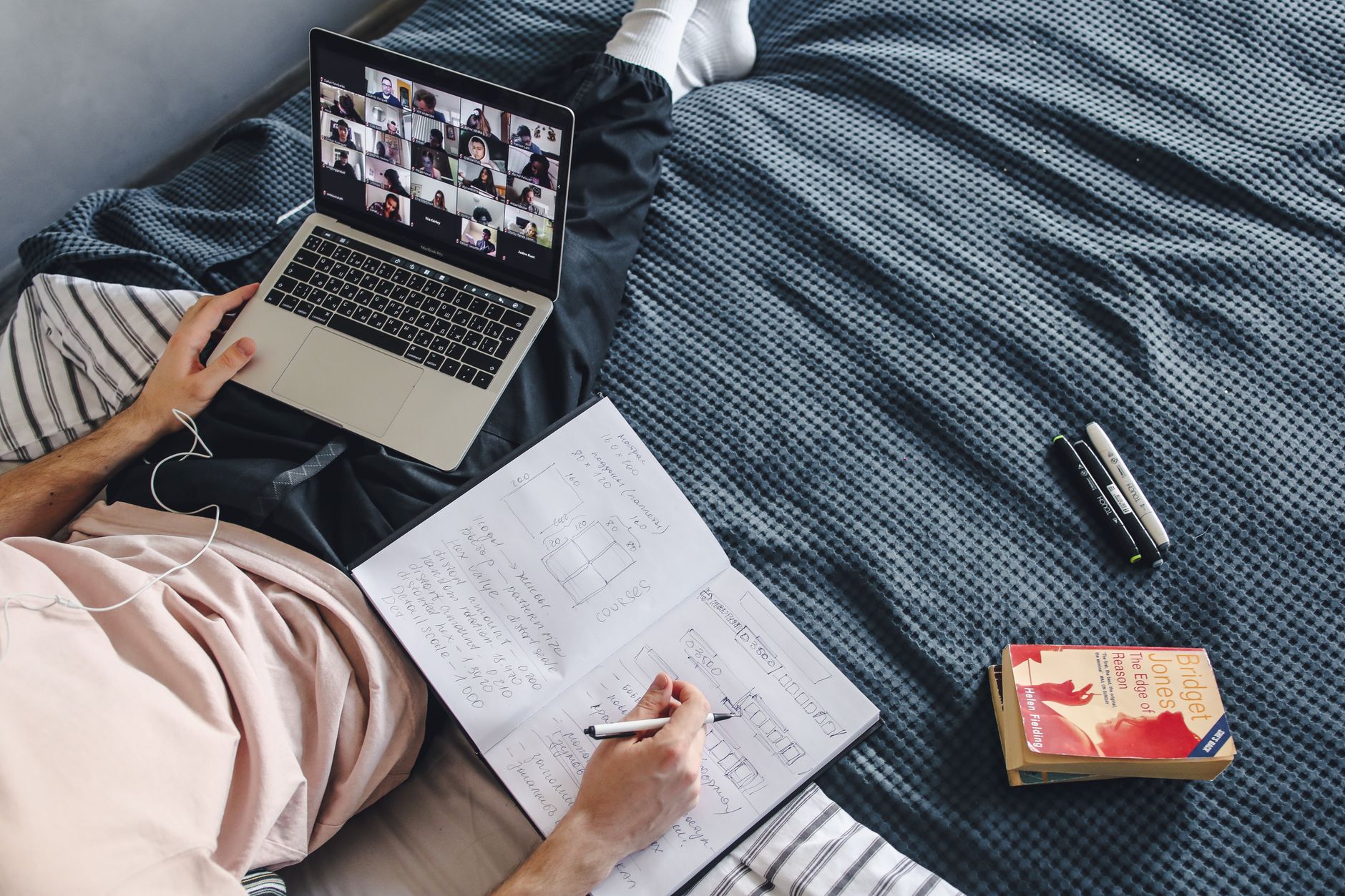 Adulte engagé dans un cours en ligne avec un ordinateur portable et un carnet tout en étant assis dans un cadre de lit confortable.