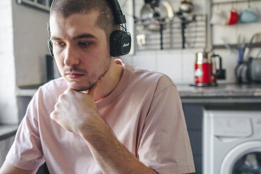 Young man with headphones sitting in a modern kitchen, thinking deeply.