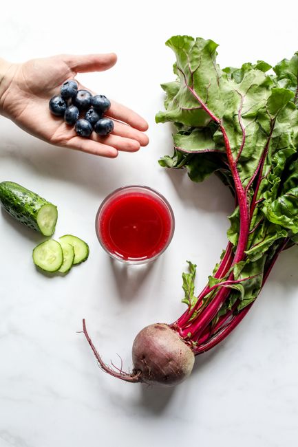 Hand holding beet juice glass with fresh beets and greens nearby