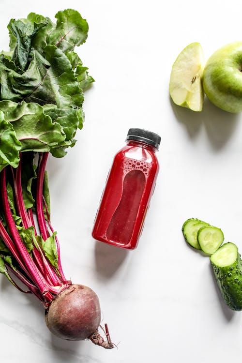 Free Red Juice in Bottle Beside Beetroot, Apple and Sliced Cucumber Stock Photo