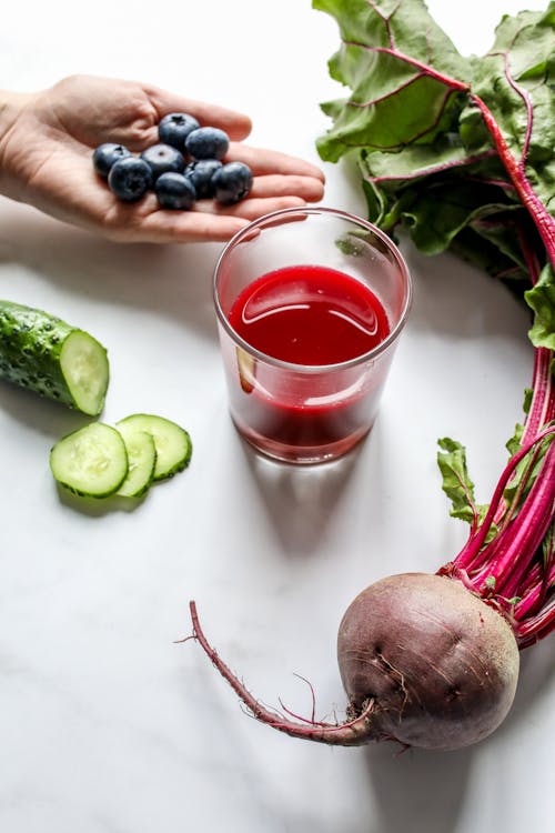 Blueberries on Person's Hand Beside Juice in Glass, Beetroot and Cucumber