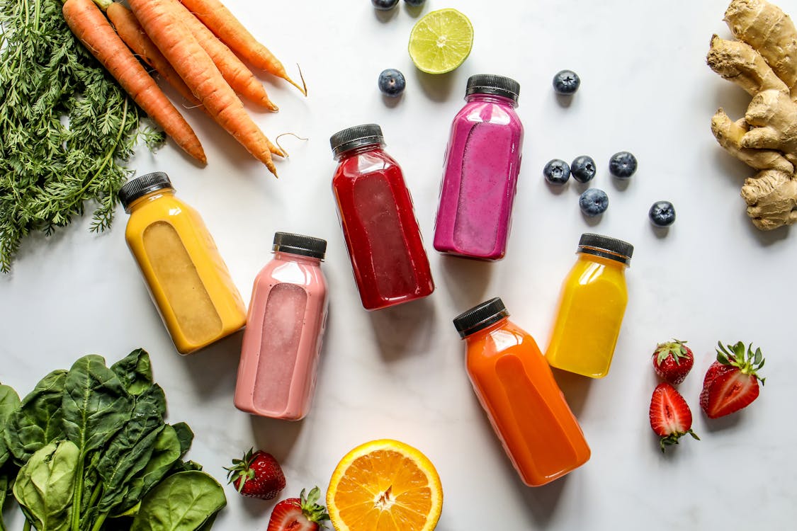 Free Colorful Bottles with Smoothies Beside Carrots, Ginger, Leaves and Berries Stock Photo