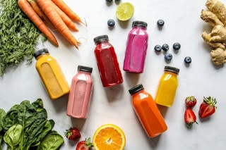 Colorful Bottles with Smoothies Beside Carrots, Ginger, Leaves and Berries