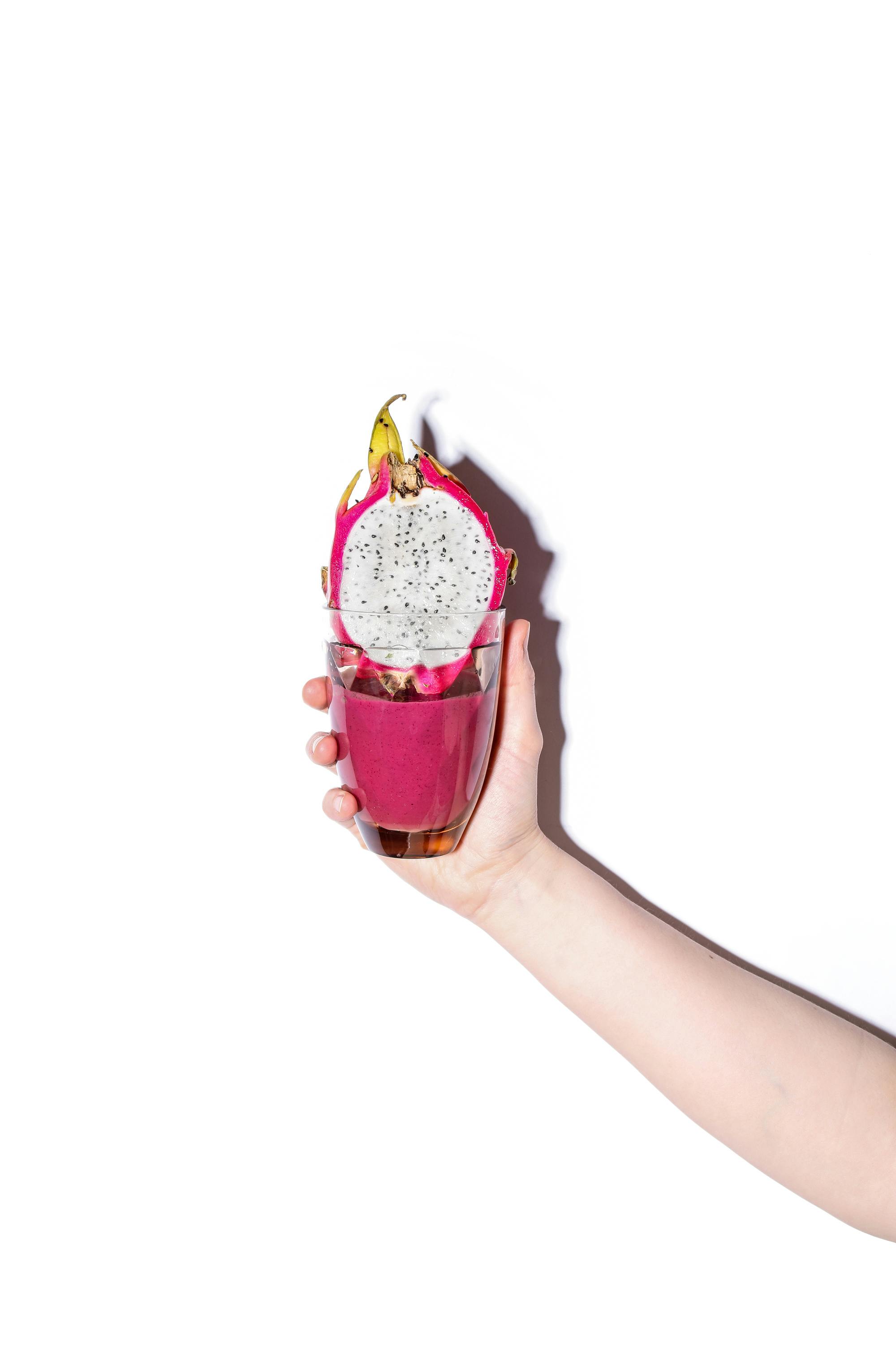 person holding glass with smoothie and dragon fruit