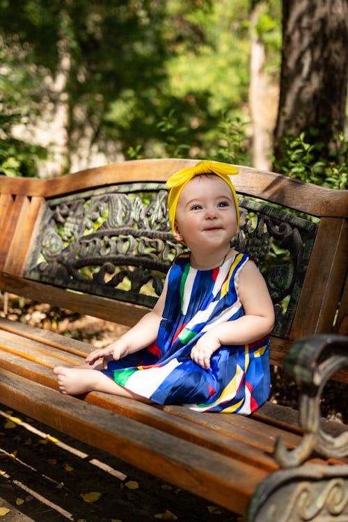 Girl in Blue Dress and Yellow Bow Sitting on Wooden Bench