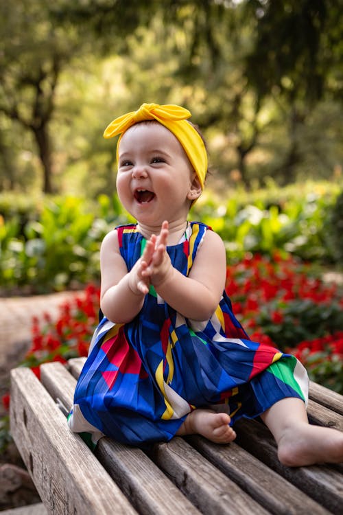 Free Girl in Blue Dress and Yellow Bow Sitting on Wooden Bench and Laughing  Stock Photo