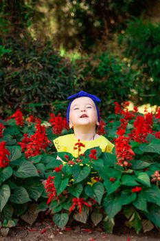 在阳光明媚的花园里，小孩子闭着眼睛，享受红花间的户外生活