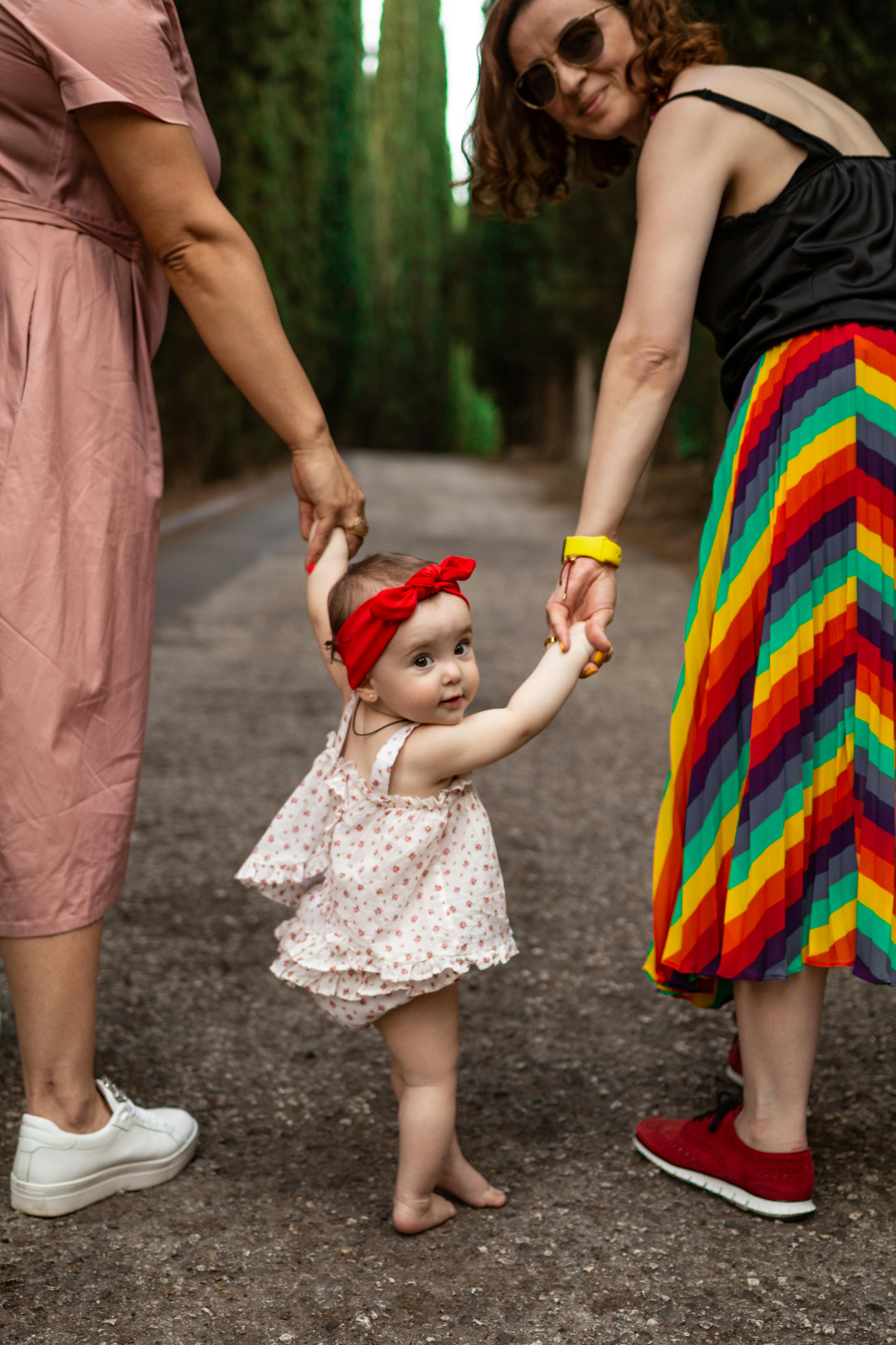 two women holding hands of girl in floral shirt walking barefoot