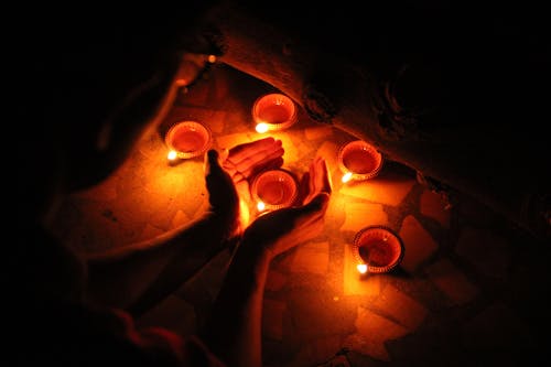 From above crop anonymous person burning candles and standing with candleholder between hands in darkness