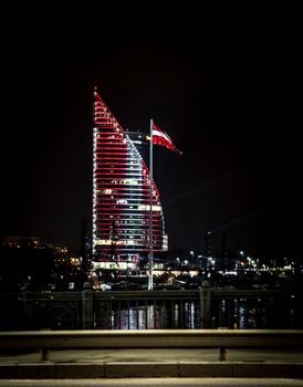 夜晚，拉脱维亚的城市里，现代摩天大楼被鲜艳的灯光和国旗照亮