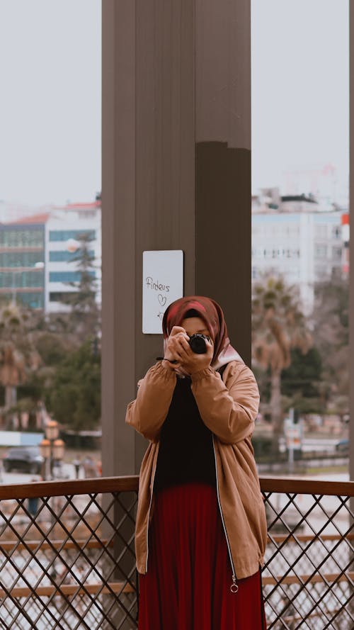 Free Unrecognizable Muslim female wearing headscarf and modest clothes taking pictures on modern photo camera while standing on street in urban environment Stock Photo