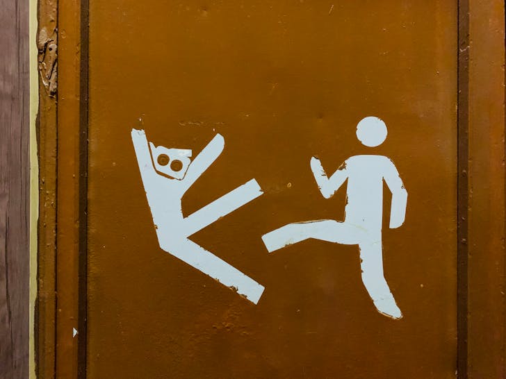 White symbolic human figures drawn on weathered brown door illustrating person kicking visitor out