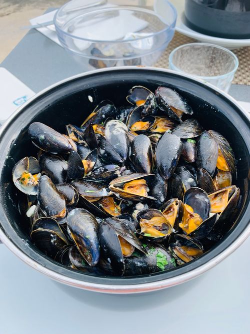 Free From above of big steel bowl full of mussels placed on dining table near glassware Stock Photo