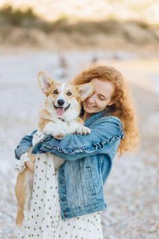 在海滩度过一天的女人，穿着牛仔夹克，抱着她的柯基犬微笑