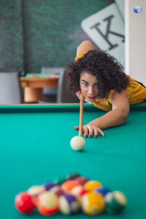 Positive focused Hispanic female in casual wear bending over billiard table with pool stick and preparing to push ball