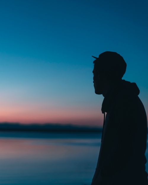 Free Side view of silhouette of unrecognizable male in cap admiring view of calm lake in sunset Stock Photo
