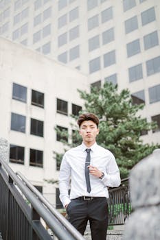 Young man in formal attire standing confidently in front of modern urban building.
