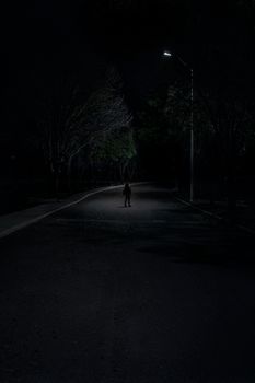 路灯下，一个孤独的人影不祥地站在黑暗的道路上