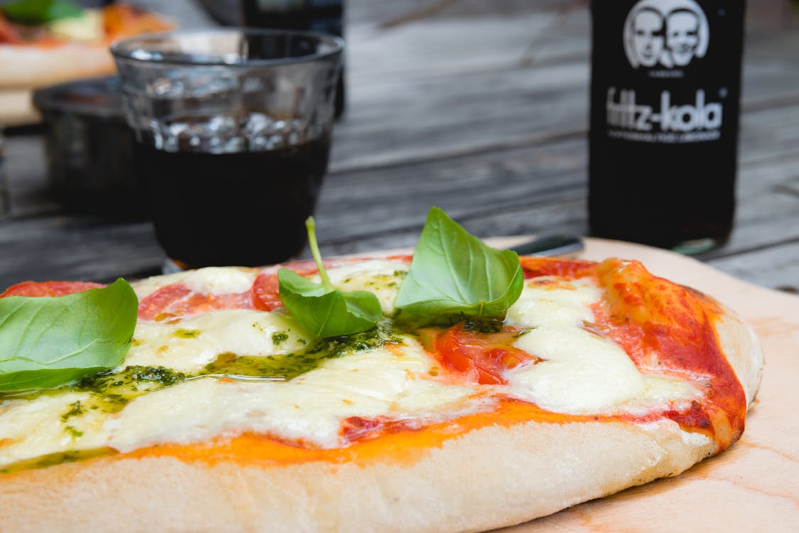 Pizza Top With Green Leafy Vegetable Near Glass of Black Liquid