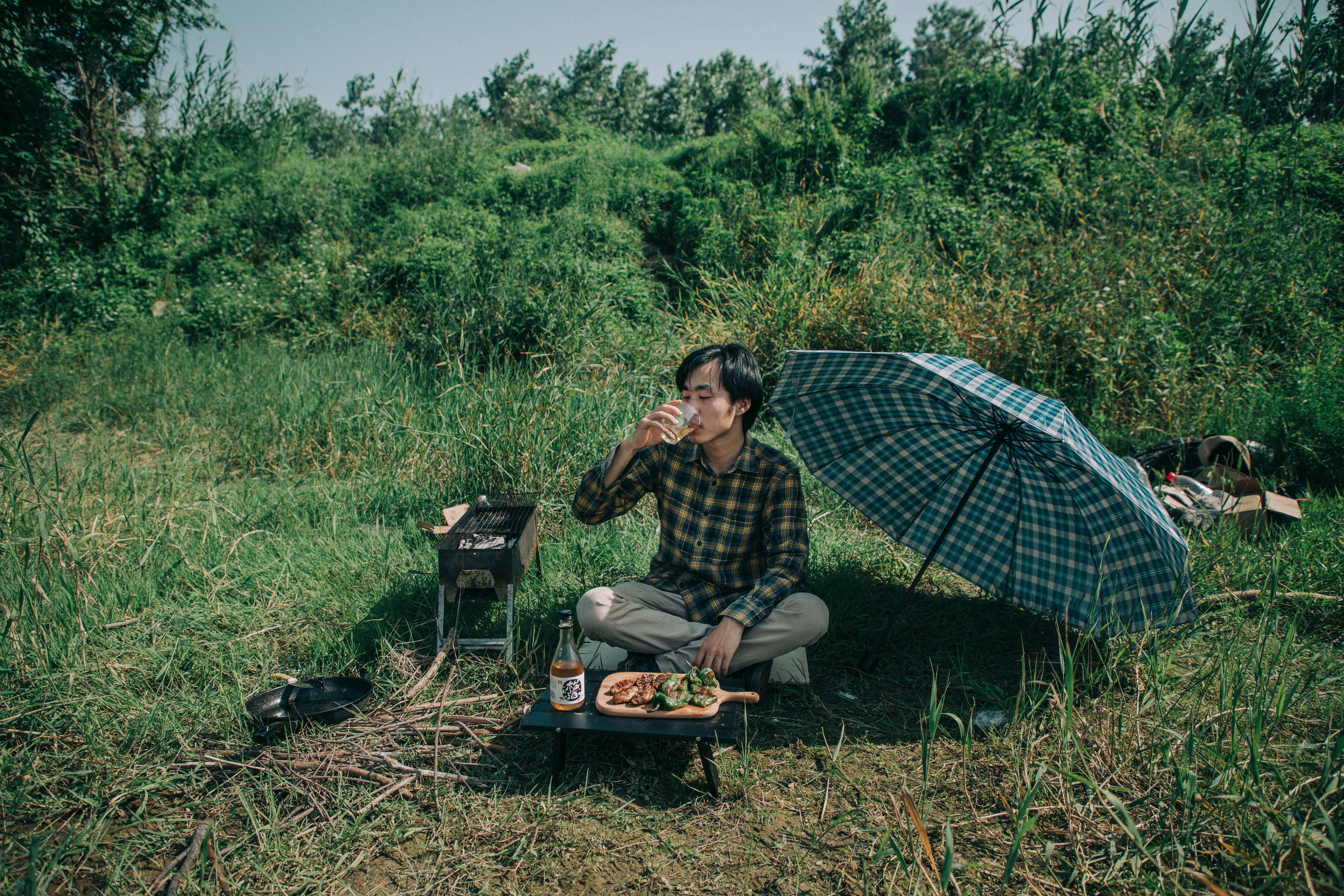 photo of man drinking while sitting on grass field