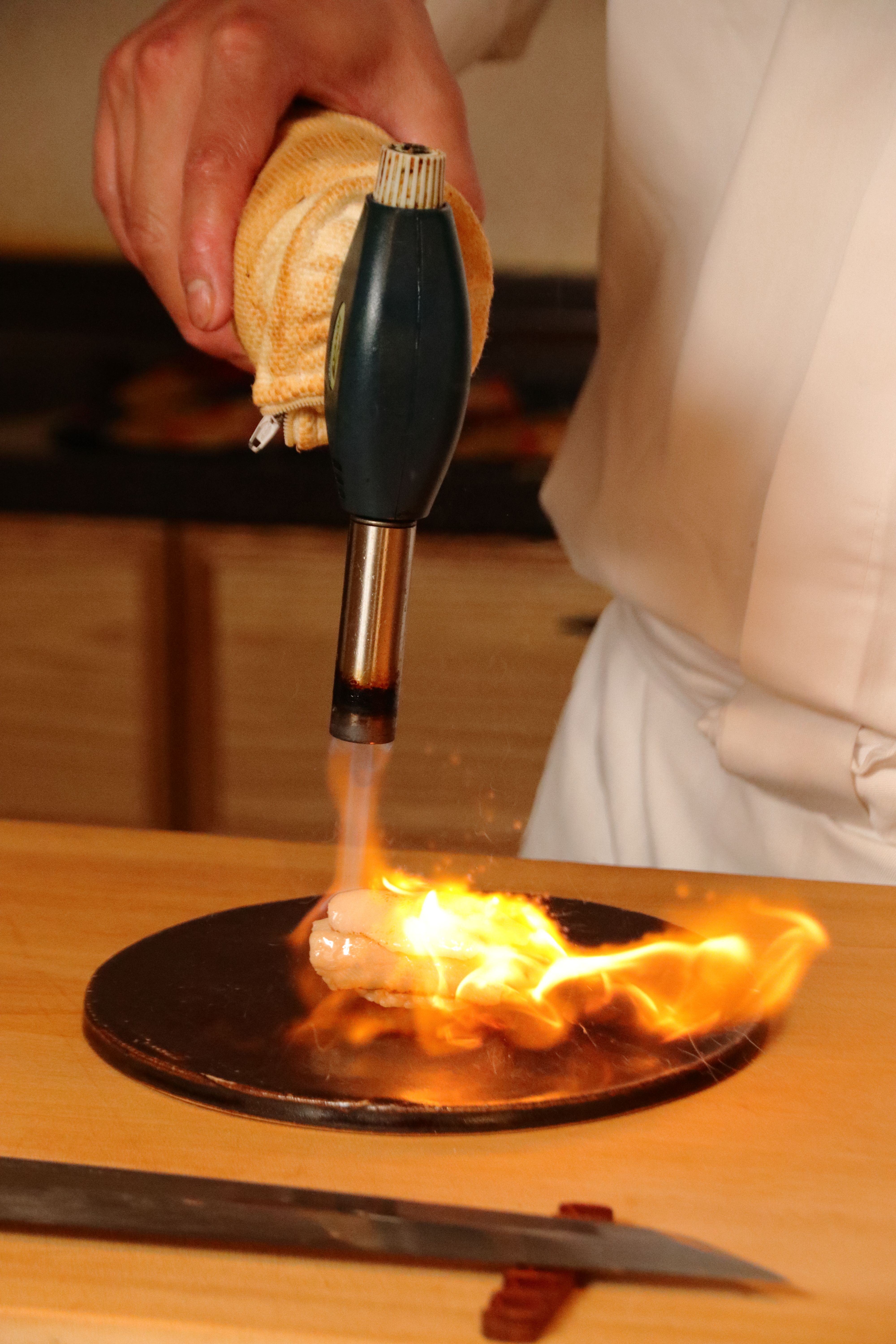 Chef using blow torch to flame dish indoors, capturing cooking artistry.