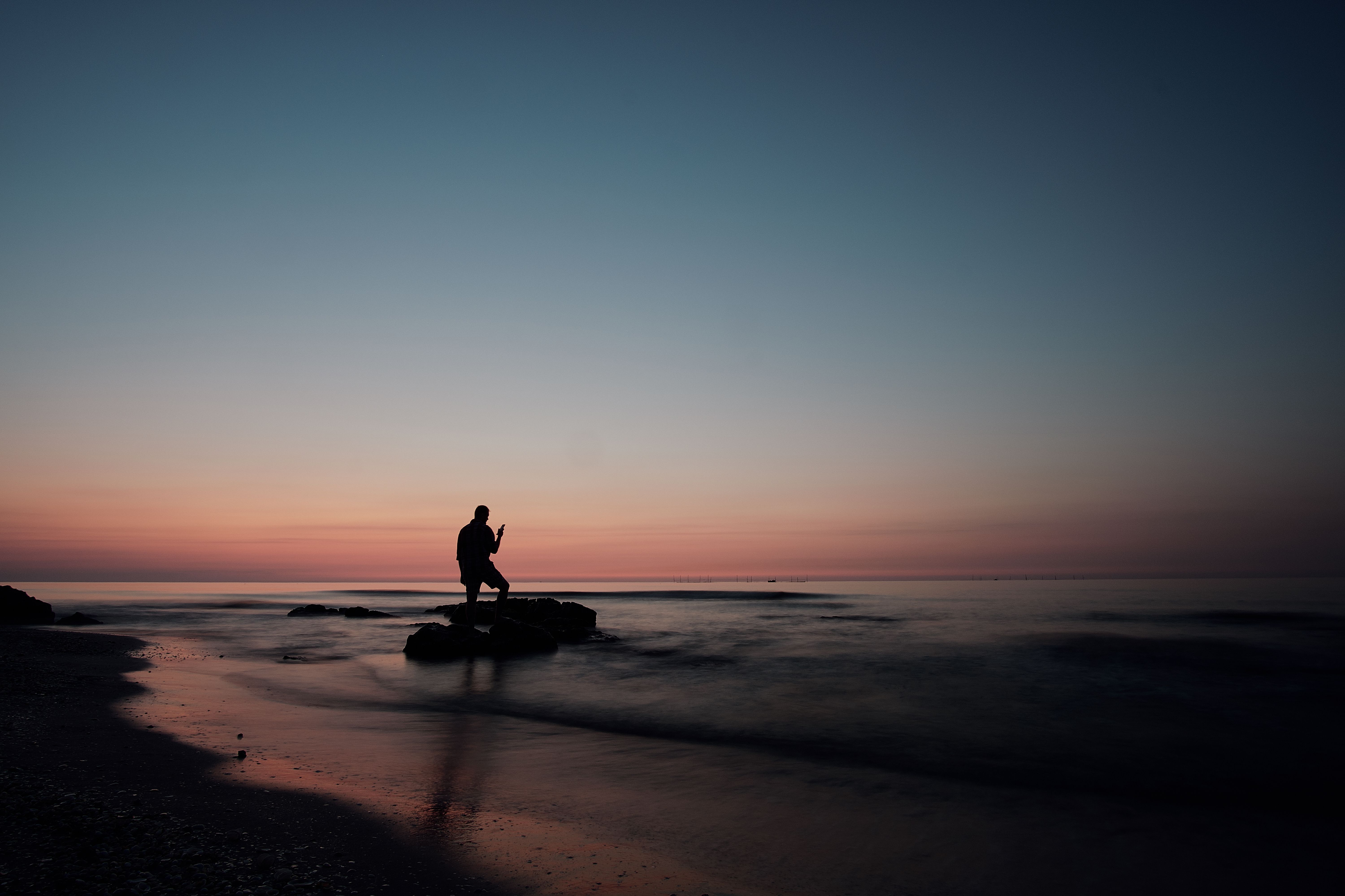 Silhouette of Person Standing on Beach during Sunset · Free Stock Photo