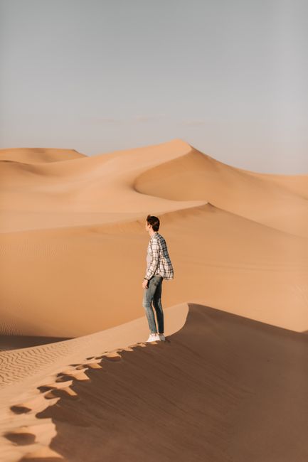 A man explores the vast sand dunes of the Abu Dhabi desert under a clear sky.