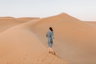 一名女子身穿花卉连衣裙，独自走在阿布扎比沙漠的沙丘上