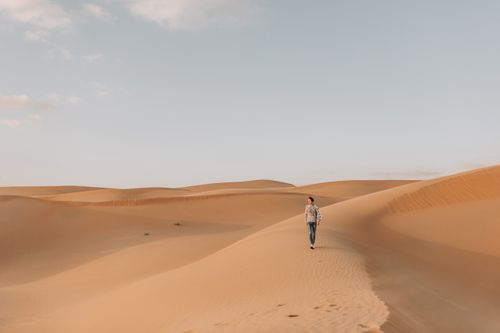 Free A lone traveler walks amidst the vast sand dunes of Abu Dhabi's desert under a clear sky. Stock Photo