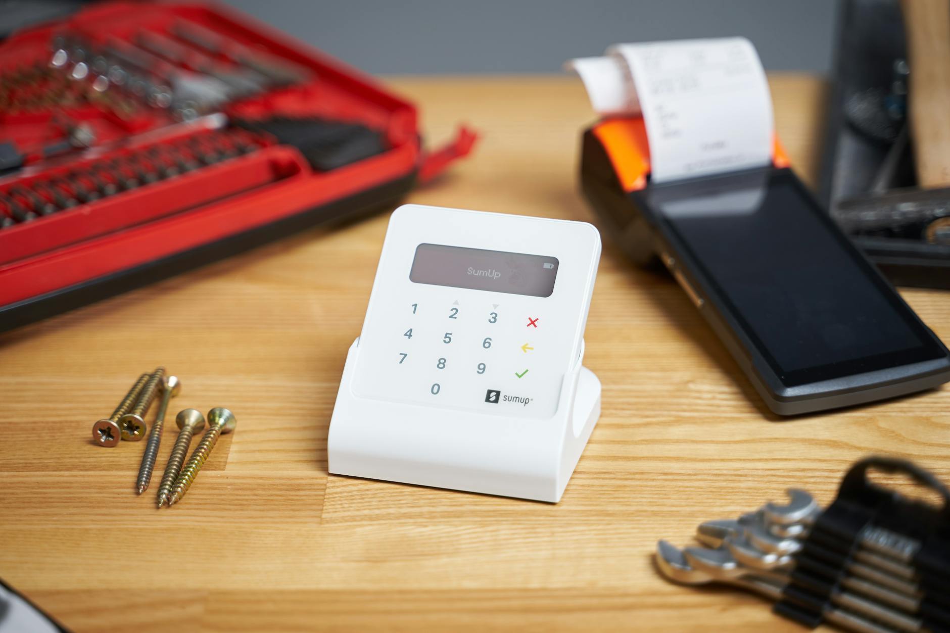 Selective focus of white contemporary calculator surrounded by cash register and tools for repair and building on beige wooden table in bright room