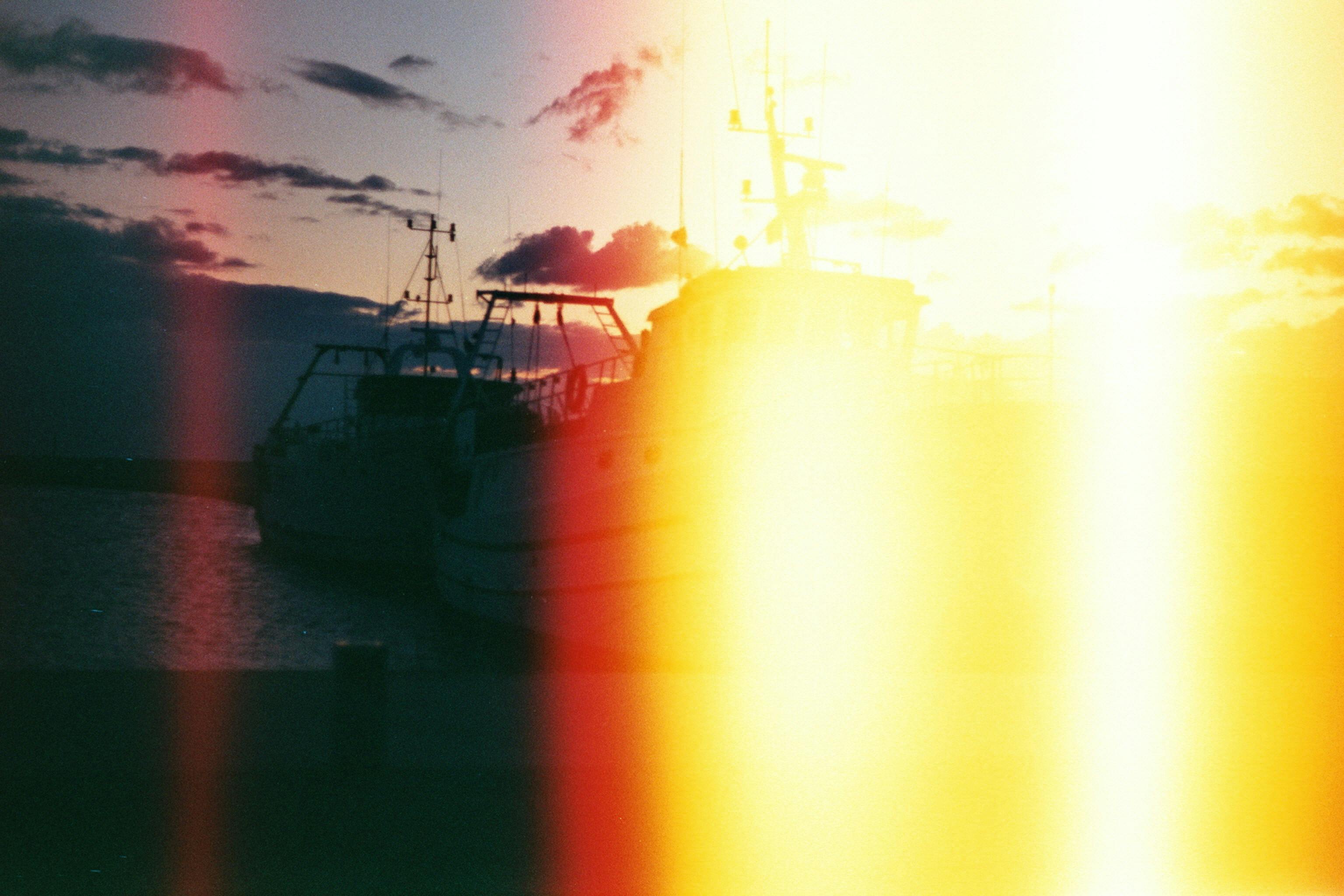 Atmospheric view of a harbor at sunset with visible light leaks creating a dreamy effect.