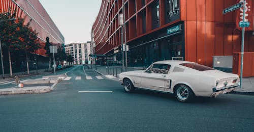 Free White Coupe on Road Near Red Building Stock Photo