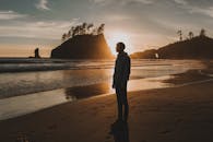 日落时分，海滩上一个人站在悬崖边的剪影，与海浪相伴