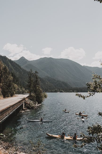 Canoes and kayaks on a serene mountain lake, surrounded by lush trees and majestic peaks.