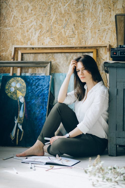Free Photo of Woman Wearing White Long Sleeves and Black Pants While Sitting on Floor Looking Pensive Stock Photo