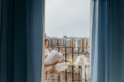 一个女人喜欢在阳台上看书，旁边有一只白猫和一杯果汁