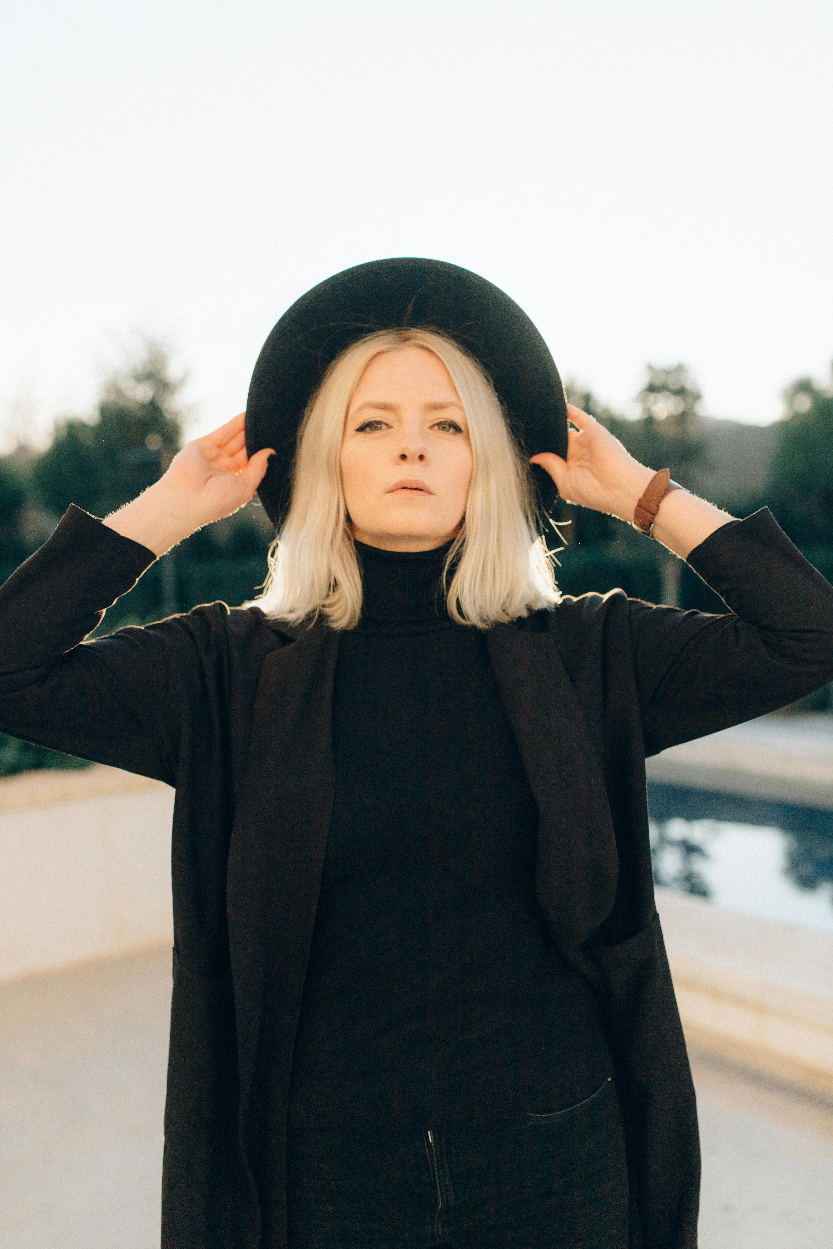 自信的女人在黑色服装与帽子，在一个阳光明媚的日子在户外摆姿势