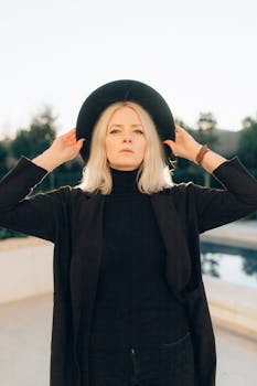 一个自信的女人，在阳光明媚的日子里，身着黑衣、头戴帽子，在户外摆着姿势