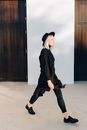 一位穿着黑色服装和帽子的时尚女人自信地走在木门上