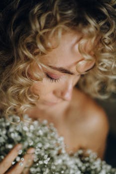 柔和的焦点特写肖像中，一位卷发女子手持白花，唤起一种宁静浪漫的心情