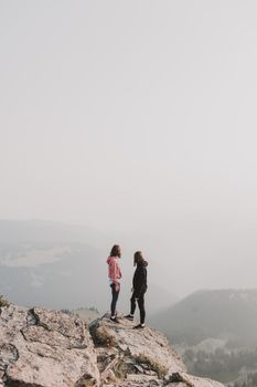 两名妇女站在晨雾笼罩的山峰上，展现着清晨的冒险与探索